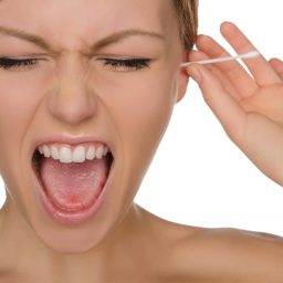 Woman sticking a qtip into her ear with a painful reaction on her face