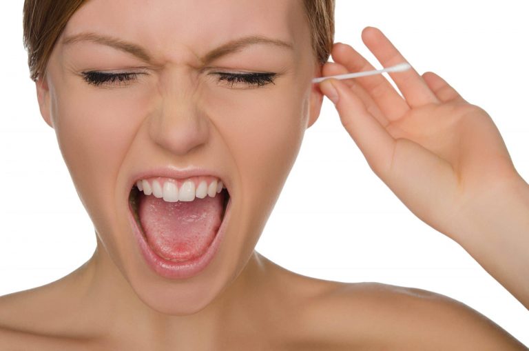 How to Safely Clean Your Ears Woman sticking a qtip into her ear with a painful reaction on her face