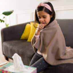Little girl sitting on the couch and coughing.