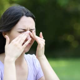Woman scratching itchy eyes or sinus in a park