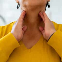 Woman with tonsillitis feeling her throat.