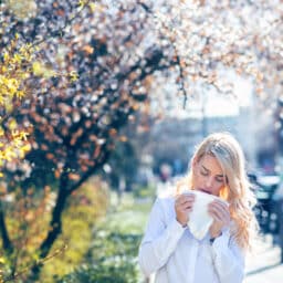 Woman sneezes near trees