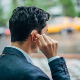 Man on the street adjusts his hearing aids, looking tired.
