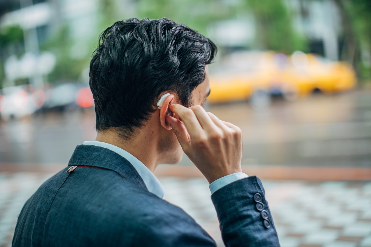 Man on the street adjusts his hearing aids, looking tired.