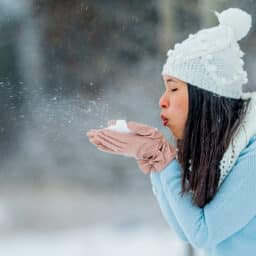 A woman blows snow from her cupped hands on a snowy winter day.